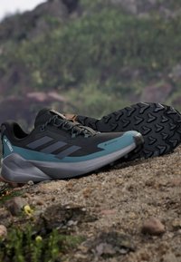 Schwarze und türkisfarbene Trail-Schuhe mit einer strukturierten Oberseite, verstärktem Zehenbereich und rutschfester Laufsohle mit einem dreieckigen Profil.