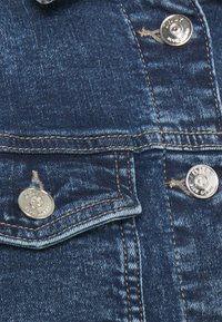 Jeansjacka med mörkblå tvätt, silverknappar och kopparbroderi. Har en bröstficka och en strukturerad krage.