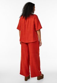 Red two-piece outfit featuring a short-sleeve top and wide-leg pants in a textured fabric, complemented by brown platform shoes.