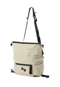 Hellbeige Umhängetasche mit verstellbarem schwarzen Riemen, vorderer Reißverschluss-Tasche und zwei schwarzen runden Knöpfen auf der unteren Vorderseite.