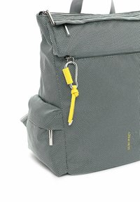 Mochila de tela tejida gris con cierre superior, bolsillo frontal, correa de acento amarilla y herrajes plateados. Forma rectangular, superficie texturizada.