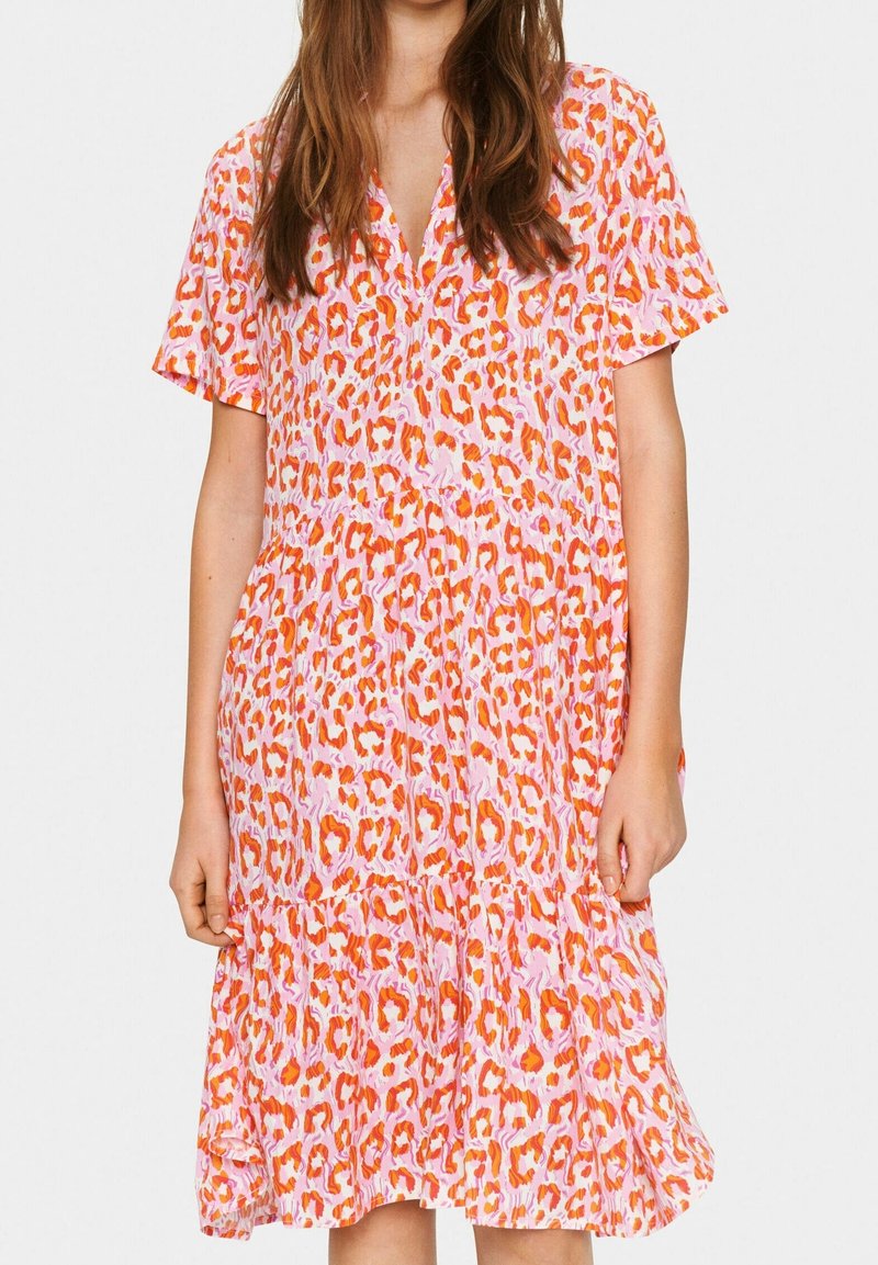 Femme portant une robe courte à manches courtes, longueur au genou, avec un motif léopard orange et rose et un col en V.
