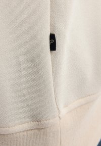 Crème katoenen sweatshirt met een gestructureerde afwerking, contrasterende beige ribbelzoom en een klein zwart merketiket op de naad.