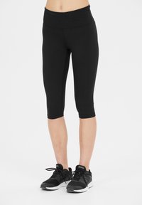 Svarta capri-leggings i stretchigt material, med hög midja och en mjuk textur, kombinerat med svarta träningsskor.