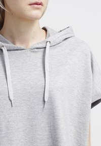 Felpa con cappuccio grigia chiara caratterizzata da una vestibilità rilassata, maniche corte e dettagli con cordino sul collo. Tessuto morbido.