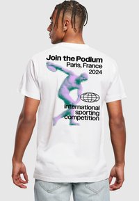 Bílá bavlněná tričko s digitální grafikou postavy v purpurové a zelené barvě, s černým textem propagujícím sportovní soutěž 2024 v Paříži.