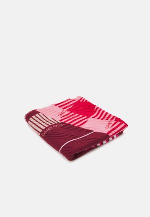 Écharpe pliée avec des motifs géométriques rouges, roses et bordeaux et des rayures diagonales sur un fond blanc.