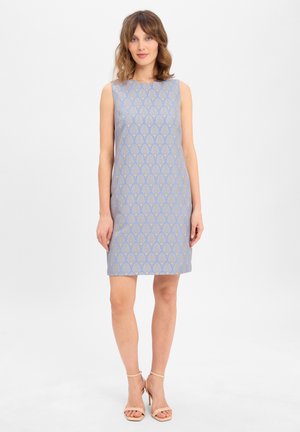 Robe sans manches de couleur bleu clair avec un motif géométrique doré. Coupe droite, mi-longueur, fabriquée dans un tissu lisse. Talons nus.