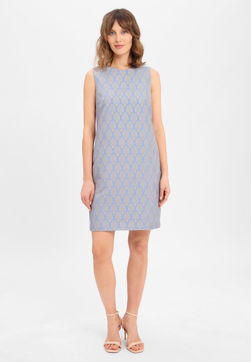 Robe sans manches de couleur bleu clair avec un motif géométrique doré. Coupe droite, mi-longueur, fabriquée dans un tissu lisse. Talons nus.