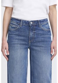 Jeans di denim blu a vita alta con una vestibilità comoda, dotati di chiusura con zip, design con cinque tasche e una leggera sfumatura per aggiungere texture.