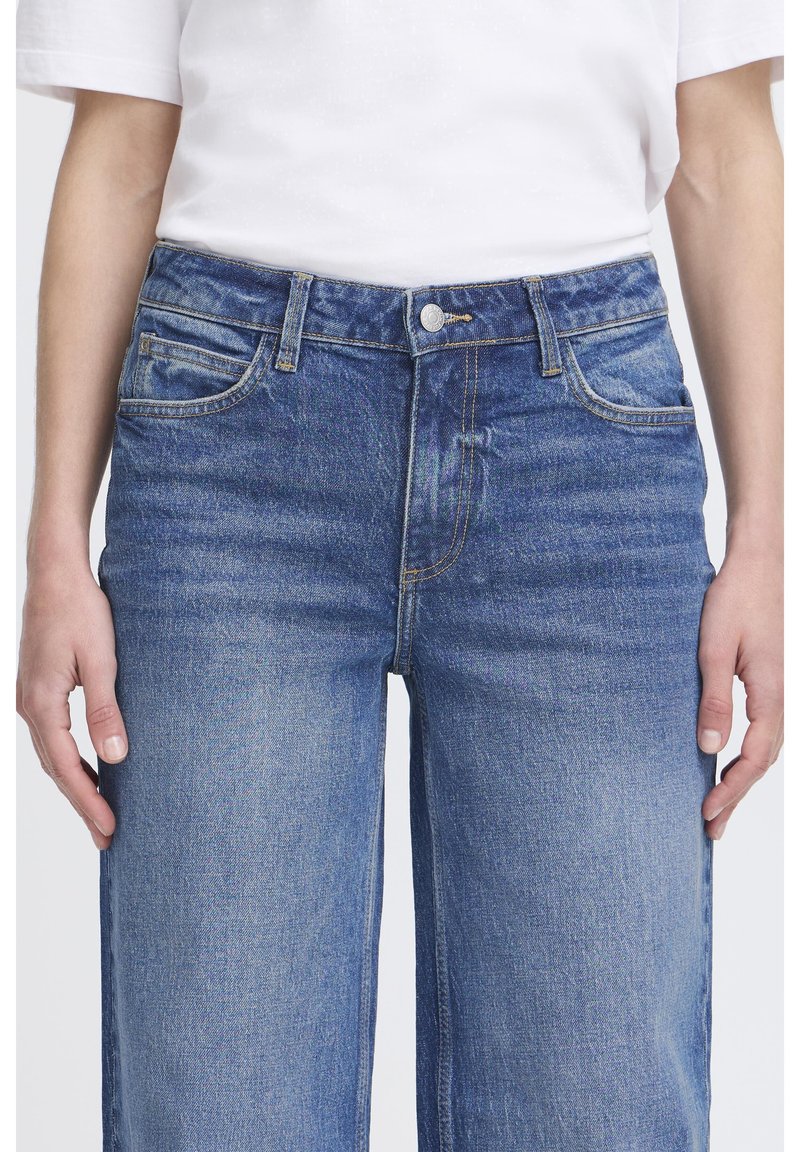 Jeans di denim blu a vita alta con una vestibilità comoda, dotati di chiusura con zip, design con cinque tasche e una leggera sfumatura per aggiungere texture.