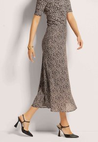 Leopardenmuster Kleid mit tailliertem Oberteil und ausgestelltem Rock; fließender Stoff, knielang. Getragen mit schwarzen spitzen Absatzschuhen und einem goldenen Armband.