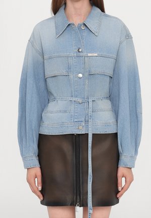 Lyseblå denimjakke med bred krave, sølvknapper, bælte og lange puffede ærmer, båret over en sort lædernederdel med lynlås foran.