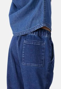 Pantaloni in denim blu scuro con vita elastica, dotati di una tasca posteriore singola e una vestibilità comoda. Il tessuto presenta una leggera trama.