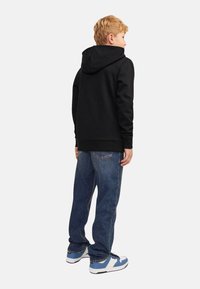 Black hoodie with a kangaroo pocket and drawstring hood, paired with blue denim jeans and blue-and-white sneakers. Casual fit, simple design.