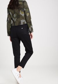 Zelená vzorovaná bunda s abstraktním designem, spárovaná s černými zúženými kalhotami a bílými teniskami, která ukazuje neformální outfit.
