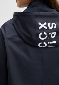 Marineblaue Kapuzenjacke mit glatter Textur, Netzfutter und auffälligem weißen Branding auf der Rückseite mit geschwungenen Details.