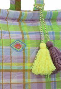 Borsa a tracolla trapuntata con un motivo a quadri multicolore in verde, giallo e viola. Include un'etichetta a patch e due frange gialle e viola.