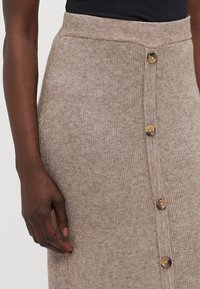 Beige ribbete strikket skjørt med høy midje, med gullknapper foran og en jevn tekstur. Ingen andre detaljer synlige.
