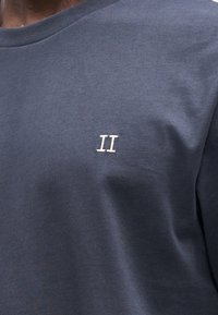 Granatowy bawełniany t-shirt z okrągłym dekoltem i małym, haftowanym logo "II" po lewej stronie klatki piersiowej. Miękki, teksturowany materiał.