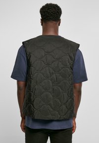 Zwarte gewatteerde vest met een gladde oppervlakte en ronde patronen, met een mouwloos ontwerp. Gecombineerd met een marineblauw shirt eronder.