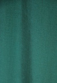 Teksturowany zielony materiał o gładkiej powierzchni, charakteryzujący się jednolitą barwą i delikatnym połyskiem, odpowiedni do odzieży lub tapicerki.