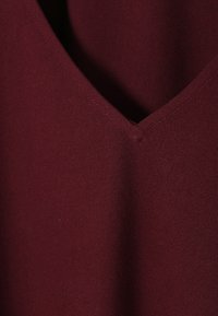 Burgundi värvi kangas, millel on sile tekstuur ja V-kaeluse disain. Õmblusdetail kaela ümber. Pehme, kerge materjal.