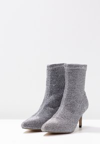 Bottines argentées avec un dessus texturé et scintillant, un bout pointu et un talon slim, offrant un ajustement serré et une doublure douce.