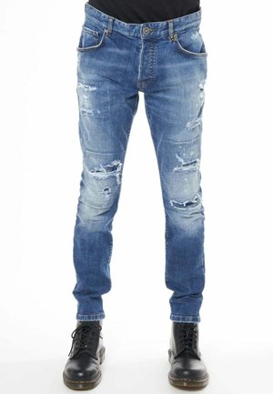 Jeans in denim blu sbiadito con strappi deteriorati, cinque tasche e una vestibilità slim, abbinati a stivali neri con lacci.