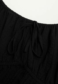 Schwarzes Stoffoberteil mit geraffter Textur und elastischem Ausschnitt. Verfügt über eine Bindeschleife und vertikale Nähte für zusätzliches Design.