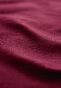 Tessuto bordeaux con una texture liscia, caratterizzato da sottili effetti ondulati e una finitura opaca, che mostra un motivo a trama stretta.