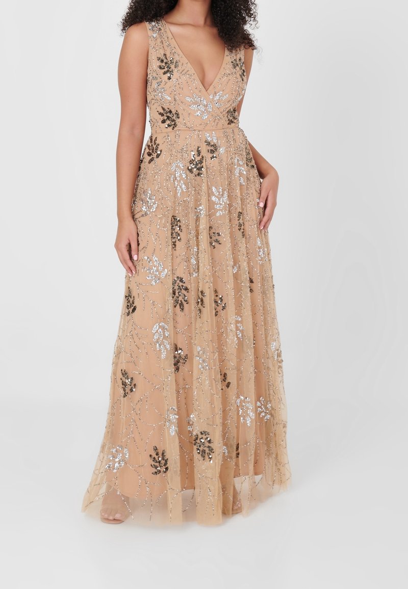 Maxi sukienka w miękkim beżu z głębokim dekoltem w kształcie litery V, skomplikowanymi, srebrnymi i czarnymi wzorami kwiatowymi wykonanymi z cekinów oraz zwiewnym, przezroczystym wierzchem.