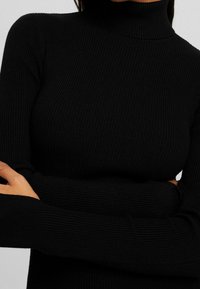 Pull à col roulé côtelé noir avec une coupe ajustée, manches longues et tissu texturé. Style simple et polyvalent.