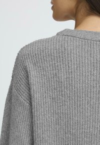 Szürke kötött pulóver, bordázott textúrával, kerek nyakkivágással és varrás nélküli vállmegoldással, hátulról nézve.