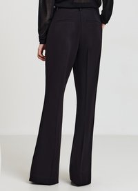 Pantalon noir évasé à texture lisse, avec une taille ajustée et deux poches arrière, s'élargissant jusqu'à une jambe large à l'ourlet.