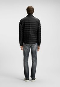 Svart puffjacka med horisontell quiltning, ståkrage och tryckknappsmuddar, tillsammans med slitna grå jeans och mörka sneakers.