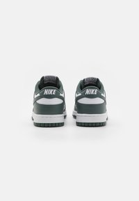 Nike Dunk sneakers in dark green and white leather, low-cut design with padded collar, rubber sole, and contrasting stitching details.