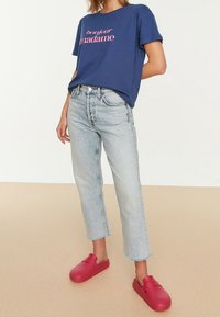 T-paita merijalkaväen sininen, jossa on vaaleanpunaisella tekstillä "bonjour madame", vaaleansiniset korkeat farkut ja punaiset puukengät pyöreällä varvasyksiköllä ja sivuventtiileillä.