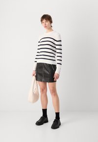 Strikkegenser med marineblå striper, paret med et svart skinn miniskjørt med en søm foran. Holder en myk, lys rosa håndveske. Svarte sko og sokker.