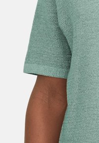 Müntroheline kudum, millel on lühikesed varrukad, tekstuurse mustriga ja lõdva istuvusega. Materjal näeb välja kerge ja hingav.