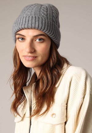 Bonnet en tricot gris avec un motif en côtes et un bord côtelé. Texture douce avec un dessus arrondi. Porté avec une veste en corduroy de couleur crème.