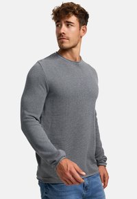 Grå langermet genser med teksturert strikkemønster, rund hals og tettsittende ermer, kombinert med blå denimjeans.