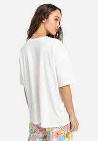 Hvid oversized t-shirt lavet af blødt stof, med rund halsudskæring og korte ærmer, parret med farverige bukser med blomstermønster.