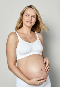 Weißer Still-BH mit verstellbaren Trägern, nahtlosem Design und gerafftem Stoff in der Mitte. Das Modell hat einen sichtbaren Babybauch.