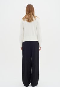 Bílý svetr s žebrovaným lemem a manžetami, zkombinovaný s volnými černými kalhotami. Hladká látka s uvolněným střihem, zobrazeno zezadu.