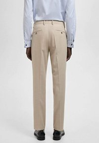 Pantaloni beige su misura con design a gamba dritta, dotati di due tasche posteriori e un tessuto morbido, abbinati a una camicia elegante azzurro chiaro.