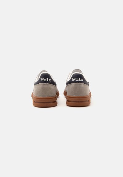Pair of gray suede sneakers with brown soles and black heel tabs showing "Polo" brand text from the back on a white background.