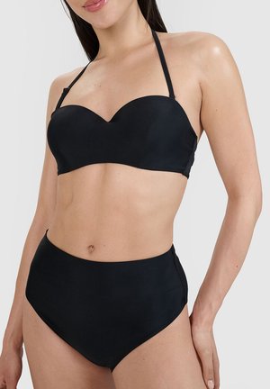 Kobieta ubrana w czarny bikini z wysokim stanem, górą bez ramiączek z dekoltem w kształcie serca oraz paskiem wiązanym na karku na jednolitym tle.
