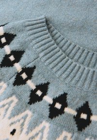 Maglione lavorato a maglia di un azzurro chiaro con colletto a coste, caratterizzato da motivi a rombi in bianco e nero. Texture morbida, design grafico dettagliato.