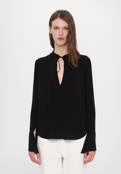 Blouse noire à manches longues avec un col en goutte d'eau, plis texturés et poignets ornés. Tissu léger avec un design fluide.
